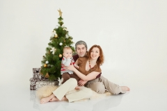 Happy family sitting at the new-year tree on white studio